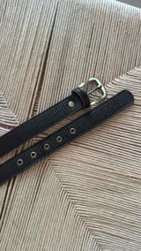 Cinturón negro de cuero sintético con hebilla cuadrada dorada y ojales metálicos.