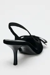 Zapato destalonado de terciopelo negro con tacón fino y adorno de lazo en la parte delantera.