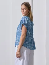 Blusa celeste estampada con motivos de playa, con cuello a la base y escote en V. Mangas cortas con detalle fruncido.