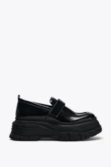 Zapato tipo mocasín negro con plataforma y suela track. Presenta tira ajustable adherente y tirador trasero.