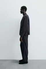 Pantalón de vestir negro de corte relaxed fit confeccionado en tejido con lana. Cuenta con bolsillos frontales y traseros de doble vivo con botón. Cierre frontal con cremallera y botón.