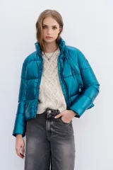 Campera puffer metalizada color azul petróleo, con cuello alto, cierre frontal y bolsillos con cierre. Tiene ajuste interno en el ruedo.