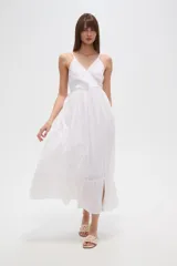 Vestido largo blanco de algodón con broderie, escote en V cruzado y breteles finos. Presenta un corte entallado en la cintura con elástico y falda fluida con tajo lateral.