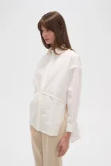 Camisa blanca de algodón, holgada, con cuello camisero, cierre frontal con botones y mangas largas.