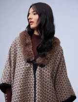 Ruana de tejido suave, color beige y marrón con estampado geométrico repetitivo. Posee cuello con aplique de piel sintética marrón y ribetes negros. Se combina con un suéter marrón de manga larga con botones en el puño.