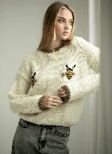 Sweater tejido a mano en lana merino color crudo, con cuello redondo marrón y diseño de abejas bordadas en el frente.