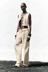 Pantalón de tiro alto color beige con finas rayas verticales negras, pernera ancha y cinturón trenzado a tono.