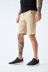 Bermuda color beige de corte chino, con bolsillos laterales, cierre con cremallera y botón, presillas para cinturón y logo bordado. Confeccionada en lino y algodón.