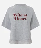 Remera gris melange de media malla con cuello redondo, mangas cortas raglán y estampado "Wild at Heart" en color bordó. El bajo de la remera cuenta con una aplicación de encaje.