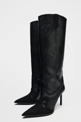 Bota alta de cuero negro con puntera fina y tacón de aguja. Diseño estilo cowboy con paneles combinados de cuero liso y gamuza.
