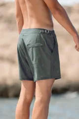 Short de baño verde militar con estampado de palmeras, pretina fija con hebillas metálicas laterales, botón a presión, cierre frontal, tres bolsillos (dos laterales y uno trasero), tela con spandex de secado rápido e interior de mesh hipoalergénico.