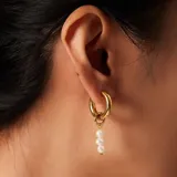 Par de aros dorados con perlas irregulares. Uno de los aros es un aro tipo argolla con perlas incrustadas, y el otro es un aro tipo argolla con tres perlas colgando.