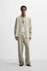 Camisa color arena de lino con cuello abotonado, manga larga con puños abotonados, corte regular y bajo con aberturas laterales.