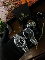 Reloj Rolex Datejust plateado con esfera negra, indicador de fecha y malla de acero inoxidable.