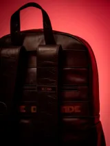 Mochila de cuero color marrón oscuro con detalles en rojo. Tiene un compartimento principal con cierre de cremallera, bolsillo acolchado interior para laptop de 15", bolsillo interior con cierre, un bolsillo frontal con cierre, bolsillos laterales, pasador en la parte de atrás para maleta, bolsillo trasero con cierre cremallera y correas ajustables. El forro interior tiene diseño Dark Side.