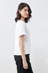 Remera blanca de manga corta con cuello redondo y botón metálico en los puños.