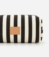 Neceser rectangular de tela con estampado de rayas verticales anchas en blanco y negro. Posee cierre de cremallera con tirador de borla negra y un parche de cuero sintético con un logo grabado en el frente.