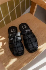 Sandalias tipo mule de cuero color marrón chocolate, con diseño de tiras anchas cruzadas y suela plana.