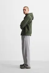Sudadera negra relaxed fit de algodón compacto con interior en rizo, cuello con capucha ajustable, manga larga, bolsillos frontales tipo canguro, acabados en rib y cierre frontal con cremallera.