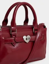 Cartera mini city de cuerina color rojo, con doble asa corta, correa regulable y desmontable, cierre superior y broche metálico de corazón.