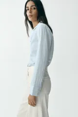 Camisa celeste con rayas verticales en blanco y amarillo, de corte entallado, cuello solapa y manga larga.