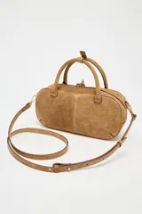 Bolso mini marrón de serraje con estilo bowling, doble asa corta y correa bandolera extraíble. Tiene pespuntes en el cuerpo, bolsillo interior con cremallera y cierre con cremallera.