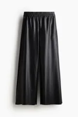 Pantalón jogger negro de corte amplio, confeccionado en tejido revestido tipo cuero sintético, con cintura elástica fruncida, bolsillos laterales y bajos deshilachados.