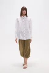 Camisa de algodón blanca, de corte ancho, con botones de madera y detalles de encaje calado en el frente, mangas y ruedo. Tiene cuello camisero y manga larga.