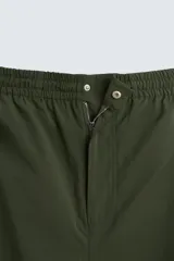 Pantalón verde militar de corte relaxed fit confeccionado en tejido técnico ligero. Cuenta con cintura elástica ajustable con cordón interior, bolsillos frontales y traseros con solapa, pliegues en las rodillas y bajo ajustable con elástico.