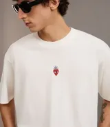 Remera boxy de algodón color crudo, con cuello redondo, manga corta y bordado de una fresa en el pecho.