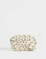 Bandolera rectangular color crema con estampado floral en negro. Tiene correa larga regulable, bolsillo frontal y cierre superior.