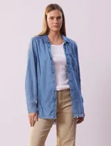 Camisa celeste de tencel marca Hester & Orchand, con cuello con solapa, escote en V y abertura central con botones. Tiene un bolsillo aplicado en la delantera y ruedo desflecado.