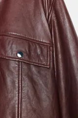 Cazadora marrón de cuero con cuello solapa y manga larga con trabillas. Tiene bolsillos de vivo y con solapa en delantero, detalle de costuras marcadas y cierre frontal con cremallera y botón a presión ocultos por sopata.