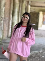 Buzo deportivo oversize color rosa, con cuello redondo y costuras expuestas en rojo. Presenta un pequeño bordado de una letra 'K' en el pecho.