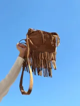 Cartera bandolera marrón de gamuza con flecos largos y correa ajustable.