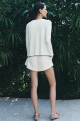 Chaqueta blanca de punto con cuello redondo y manga larga. Tiene vivos negros en el cuello, el borde frontal y los puños. Se cierra con botones en el frente.