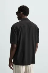 Camisa de calce relajado confeccionada en tejido fluido de mezcla de viscosa, color blanco. Presenta cuello bowling, manga corta, aberturas laterales en el bajo y cierre frontal con botones al tono.