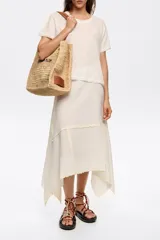 Falda midi color blanco hueso de algodón y lino, con corte irregular y vuelo. Presenta cierre lateral invisible y bordados a contraste en costuras y bajos.