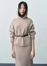 Sweater de punto color beige con capucha y cinturón fino de cuero marrón.