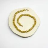 Collar de cuentas esféricas de jade amarillo, engarzadas con hilo violeta y terminaciones en acero con baño de oro.