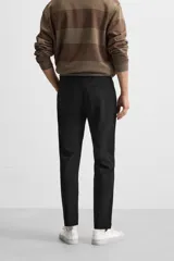 Pantalón negro de corte slim fit, confeccionado en tejido elástico. Cuenta con cintura elástica, bolsillos frontales y traseros de vivo. Cierre frontal con cremallera y botón.