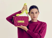 Cartera bandolera fucsia con patrón acolchado y ribete amarillo neón. Tiene asa corta trenzada color verde neón y logo "LAMODE" estampado en amarillo neón.