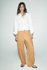 Camisa blanca de cuello redondo y escote pico, con mangas largas abullonadas y detalle de puntillas combinadas a tono en el delantero. Cierre frontal con botones forrados.