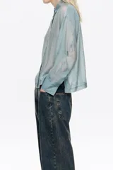 Camisa de corte boxy en color celeste, confeccionada en tejido semitransparente con apliques de pequeñas piedras brillantes. Posee cuello camisero, cierre frontal con botones y mangas largas con puños con sardineta.