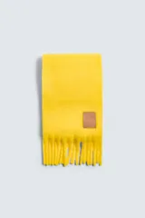 Bufanda rectangular color amarillo, confeccionada en tejido con lana y acabado cepillado. Tiene flecos en los extremos y etiqueta de cuero con logo.