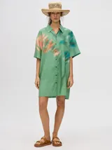 Vestido camisero corto de viscosa color verde con estampado abstracto en tonos naranja y celeste, corte oversize, manga corta, cuello camisero y cierre frontal con botones.