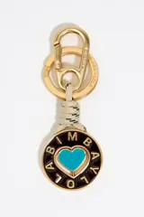 Llavero con mosquetón y anilla metálica plateada grabada con el logo de Bimba y Lola. Presenta un cordón trenzado verde con detalles en blanco que sujeta un dije circular con un corazón rojo esmaltado en el centro y el nombre de la marca calado alrededor.