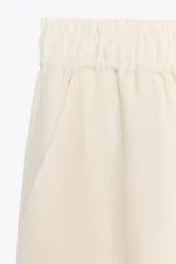 Pantalón de tiro alto color crudo, con cintura elástica, bolsillos delanteros y pernera ancha.