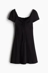 Vestido corto negro de punto acanalado con escote corazón ribeteado en encaje y cordón para ajustar en el centro del busto. Modelo de manga corta con cuerpo entallado, copas preformadas y pollera con vuelo.