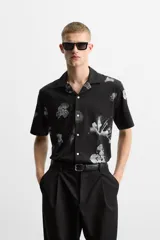 Camisa negra con estampado floral en tonos grises, de manga corta y cuello bowling.